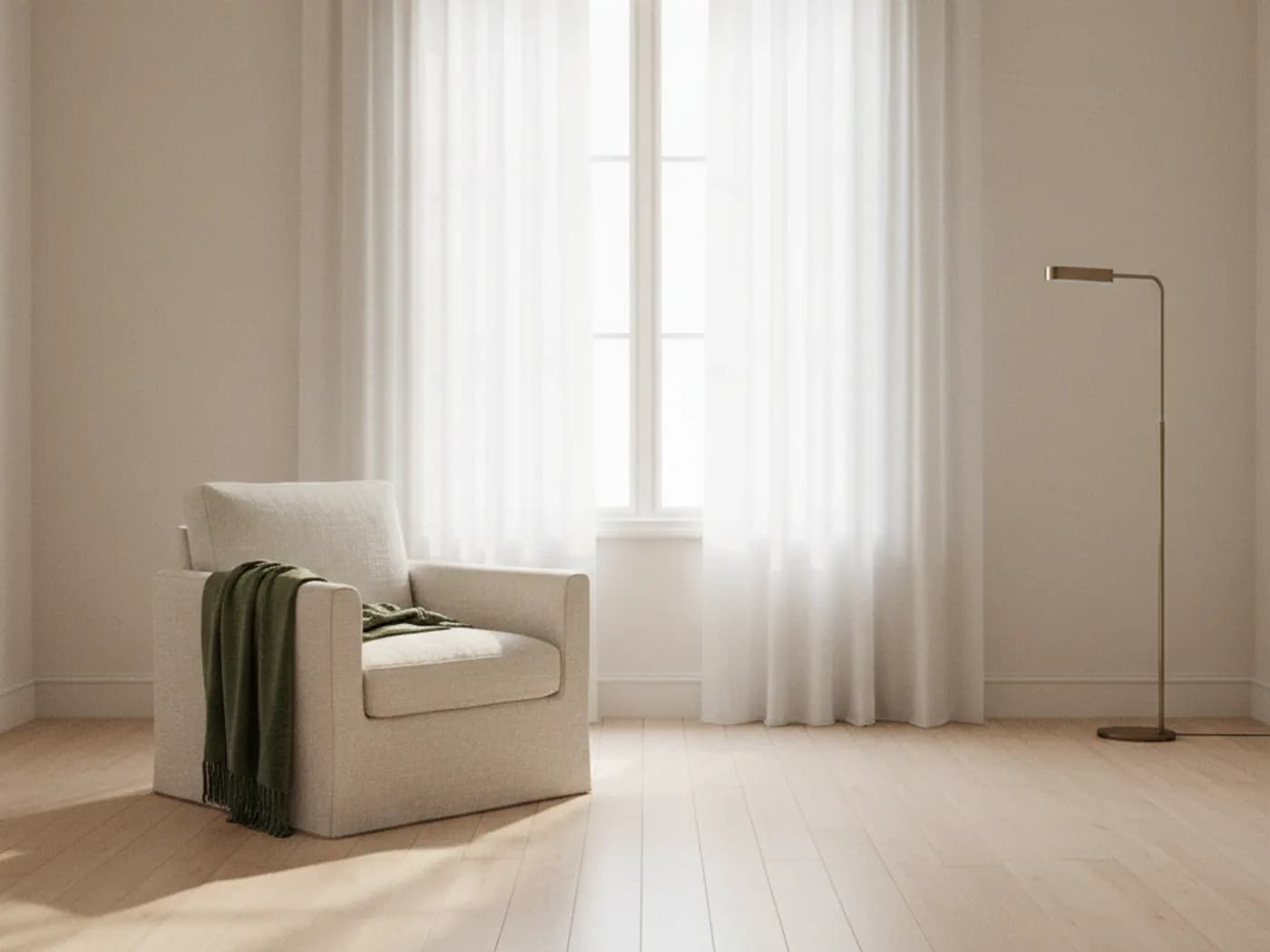 Ein heller Sessel mit grüner Decke vor einem Fenster mit weißen Vorhängen